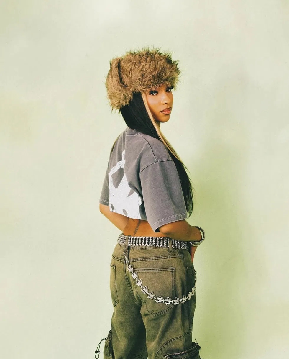 Model in a faux fur trapper hat and olive cargo pants with a chain wallet, shot from behind